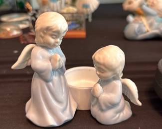 Porcelain Angel Dish — Pair of small porcelain praying angel figurines with a central shallow dish or votive cup between them. Both angels are finished in glossy white glaze with soft molded details and folded hands; one stands and one kneels. No maker's mark is visible in photos; piece shows light surface wear and small scuffs consistent with gentle use but no chips or cracks observed. Compact decorative set suitable for a mantel, shelf, or as a small votive holder.