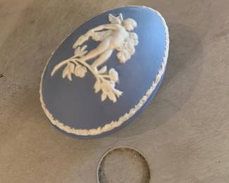 Wedgewood-Style Jasperware Oval Box — A small blue jasperware-style oval trinket box featuring classical white relief of a cherub or putto on a flowering branch. Matte blue body with crisp white applied border and central figural medallion; base shows an impressed mark but it is not fully legible in photos. Good condition with minor surface wear and a small scuff on the underside as shown. Compact decorative box ideal for jewelry or shelf display; lightweight and collectible-looking.