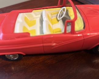 Red Fairlane Toy Convertible — Red Fairlane toy convertible model with white and yellow interior and clear windshield; distinctive hood ornament and 'Fairlane' script on the front. Made of molded metal and plastic components with painted red exterior and chrome-tone trim. Compact desk-top collectible suitable for display in an office room; measures approximately 7 inches long and is lightweight. Good condition with light surface scuffs and minor paint wear consistent with age and display use.
