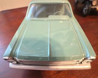 Green Ford Classic Model Car — Decorative diecast Ford model car in a pale green finish, displayed as an office accent piece. Detailed body lines, chrome-look bumpers and molded interior visible through clear windows; 'FORD' lettering on the hood front. Measures approximately 4.5 inches high by 12 inches long and 4 inches wide (small tabletop scale), making it easy to display on a desk or shelf. Overall good condition with light surface wear and minor paint blemishes consistent with age and display; wheels appear intact and it is primarily decorative.