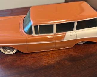 Two-Tone Brown Station Wagon — Two-tone brown and cream diecast station wagon model with chrome trim details and molded hood ornament. Solid metal construction with painted finish and plastic windows; appears to be a vintage-style collectible toy suitable for display in an office room. Measures roughly 10 inches long and shows light surface wear, small paint chips, and some scuffs on the bumpers consistent with age and display use. Overall condition is fair but intact with no major structural damage; wheels appear functional though may be slightly stiff.