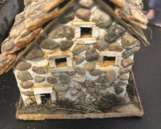 Miniature Stone Cottage Decor — Handmade-style miniature stone cottage with a bark-shingle roof and chimney, crafted from small river stones and wood elements on a thin wooden base. Decorative piece appears intact with light surface wear and some fraying at the base; good for shelf or tabletop display in a rustic or cottage-themed room. No maker or markings visible; lightweight and easy to place as an accent. Approximate compact footprint makes it suitable for display on desks, mantels, or in terrarium-style vignettes.