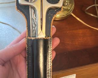 Embroidered Handle Shears with Sheath — Heavy-duty dressmaker shears with an engraved/embroidered decorative handle plate and black leather sheath. The blades and handles are polished metal with visible tooling on the inner handle plate; the sheath shows edge wear and surface scuffs consistent with age and use. Functional sewing/craft shears suitable for tailoring or display; overall good used condition with cosmetic wear to the sheath and minor surface marks on the metal.