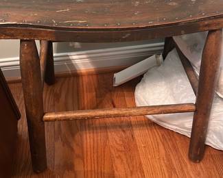 Rustic Wooden Stool — Simple rustic wooden stool with a gently curved seat and round peg legs, well suited for a bedroom or casual seating. Constructed of solid hardwood with a dark stained finish and visible wear, dings, and surface scratches consistent with age and use. Compact footprint makes it easy to move; estimated dimensions provided for reference. Overall sturdy but shows cosmetic distress and finish loss—great for restoration or as a farmhouse accent.