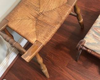 Rush Seat Wooden Stool — Small rustic wooden stool with woven rush seat and turned legs. The rush seat shows typical wear and slight looseness at one corner; the painted wood frame has scuffs and surface loss consistent with age and use. Solidly built with classic spindle-style turned legs and stretchers, suitable as an accent seat or entryway stool after minor touch-up or re-wrapping of the rush. Compact and lightweight for easy placement.