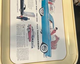 Ford Thunderbird Advertising Tray — Metal advertising tray featuring a vintage Ford Thunderbird illustration and copy celebrating the new Thunderbird; image shows a blue coupe with period figures and text. Lightweight stamped metal with a pale yellow rim and recessed printed panel; good collectible condition with minor surface wear and light scuffs consistent with age. Attractive for collectors of automotive memorabilia or mid-century advertising displays; measures compactly for wall display or serving use.