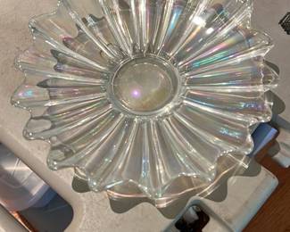 Iridescent Pressed Glass Flower Bowl — Decorative iridescent pressed-glass bowl shaped like a radiating flower with scalloped petal edges and a shallow central well. The clear glass shows a subtle rainbow iridescence in the light and appears free of chips or cracks from the provided views; surface shows light tabletop wear and faint scratches consistent with normal use. Great as a centerpiece or serving dish for wrapped candy, potpourri, or seasonal display. Measures approximately as listed and is a lightweight, easily handled accent piece.