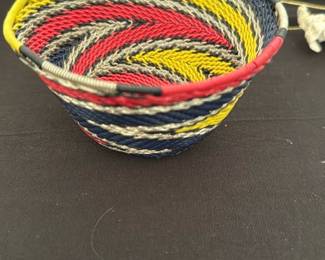 Handwoven Coil Basket Multicolor — Handwoven coil basket featuring tight spiral construction in red, yellow, navy and natural tones. Lightweight decorative bowl-sized piece with neatly wrapped rim and even stitching throughout; suitable for display or holding small items. No visible stains or breaks in the weaving from photos; shows gentle surface wear consistent with normal use. Approximately 4–5 inches across and ideal as an accent in a bedroom or tabletop vignette.