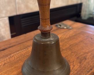 Brass School Hand Bell with Wood Handle — Solid brass hand bell with turned wooden handle, classic schoolhouse or service style. Bell shows an aged patina on the brass and light surface wear on the handle consistent with age; clapper intact and appears functional. Sturdy construction with a comfortable grip makes it desirable as a collectible or decorative piece. Good vintage condition with expected tarnish that can be polished if desired.
