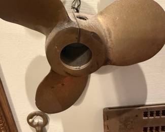 Three-Blade Boat Propeller Bronze — Three-blade bronze boat propeller shown mounted as a display piece; solid cast construction with a central hub bore. The prop is typical of small outboard or sterndrive boats and displays surface corrosion and pitting consistent with marine exposure but no major breaks or missing blades. Good candidate for restoration, nautical decor, or parts — hub bore measures roughly small-medium shaft size and blades retain original curved pitch. Sold as shown.