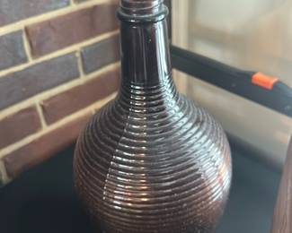 Ribbed Brown Glass Demijohn Bottle — Large ribbed brown glass demijohn-style bottle with a long narrow neck and applied ringed collar. The beehive-like horizontal ribbing and dark amber-brown color give it decorative appeal for mantel or sunroom display; photos show no visible chips or cracks but there is light surface wear consistent with age. Solid blown-glass construction, approx. medium-large size suitable as a vase or accent piece.