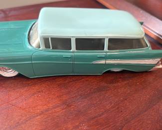 Green Chevrolet Station Wagon Model — Green Chevrolet station wagon metal model car with light green roof and darker green body, photographed on an office desk. The diecast-style toy shows molded Chevrolet script on the hood and chrome-tone trim decals along the sides, with visible wear to paint and some scuffs on bumpers and body. Approximately small display size suitable for shelf or collector display; lightweight and easy to pack. Condition is fair with surface wear, light scratches, and some paint loss consistent with age and play or display.