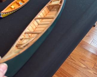 Handmade Wooden Canoe Model — Decorative handmade wooden canoe model with interior ribs and two woven-seat details. Solid wood construction with painted exterior (green) and natural wood interior; shows light surface wear and small scuffs consistent with age and display use. Good decorative condition and well-suited for bookshelf or mantel display as a nautical accent. Measures compactly and is lightweight for easy placement; no maker markings visible in photos.