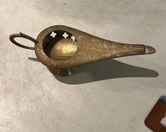 Brass Genie-Style Incense Burner — Brass genie-style oil lamp with engraved surface decoration and a looped handle; metal shows light surface patina and minor wear consistent with age. Solid-cast look with pierced quatrefoil vents around the filler well and a tapered spout typical of decorative Middle Eastern or Victorian revival pieces. Good for display as a decorative accent or as part of a collectible lamp grouping; no wick or fuel components visible. Condition is good overall with expected surface scratches and tarnish.