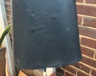 Large Black Cowbell — Heavy iron cowbell with a large flared body and original single clapper; shows surface pitting and wear consistent with outdoor/agricultural use. Solid, utilitarian construction makes it suitable as rustic decor or for collectible farm implements. No maker's marks visible in photos; finish is matte black with age-related oxidation and minor dents along the rim. Approximately palm-sized handle and roomy interior — sold as-is.