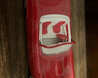 Red Convertible Toy Car — Red diecast convertible toy car with white interior and working wheels shown from multiple angles. Solid metal body with some paint wear and light surface scuffs consistent with play or display; interior and steering wheel intact. Underside shows simple stamped chassis and axle construction typical of mass-market diecast toys. Compact collectible suitable for a toy shelf or model car lot; see photos for condition.