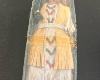 Native American Doll in Box — A handcrafted Native American style doll preserved in its original clear plastic display box. The doll wears a white dress with fringe, a yellow vest and headband, and has painted beadwork details down the front; soft moccasin-style shoes are visible. Box shows surface wear, yellowing tape and scuffs consistent with age and storage. A decorative collectible likely for shelf display; measurements and weight are estimated from photos.