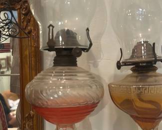 Glass Oil Lamp — Tall glass oil lamp featuring a clear blown-glass chimney and a ribbed font with a distinct red band near the base of the reservoir. The lamp has a metal burner assembly with a wick adjuster and sits on a clear flared glass pedestal base. Good decorative condition with light surface wear and patina on the metal burner consistent with age; chimney appears free of visible chips or cracks. Measures approximately 17 inches tall overall and makes an attractive display piece for classic or Victorian-style decor.