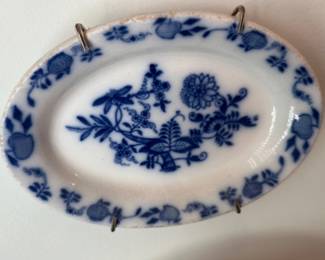 Blue White Transferware Oval Platter — Blue-and-white transferware oval platter with a central floral and foliate motif and decorative border. Made of glazed ceramic/porcelain, the piece shows light surface crazing and some rim discoloration from age; mounted on a wall display in the living room. Measures approximately 10.5 inches long by 6.5 inches wide and about 0.75 inches tall, suitable as a small serving or decorative platter. Overall condition fair with age-related wear and staining around the rim but no obvious large chips or cracks visible in photos.