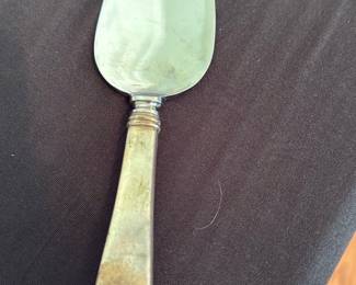 Silverplate Cake Server — Heavy silverplate cake/pie server with a tapered teardrop blade and simple rounded handle. Blade shows light surface scratches and an engraved script mark (hard to read in photos); handle has visible tarnish and wear consistent with age but no breaks. Solid, utilitarian serving piece that cleans up with polishing and is useful for parties or daily service; measures small enough for standard cakes and pies.