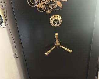 American Eagle Gun Safe Black — American Eagle gun safe in black finish with gold logo and three-spoke locking handle. Interior shows padded shelves, a vertical divider and molded rifle slots for organized long-gun storage; door has UL residential security listing and warranty label. Measures approximately 55 in tall x 24 in wide x 20 in deep (estimated) and is a heavy, floor-standing safe suitable for a home; sold from bathroom room at 1395 Charleston lane. Good condition cosmetically with normal interior shelf wear and intact locking bolts; selling as-is with no key or combination provided in photos.