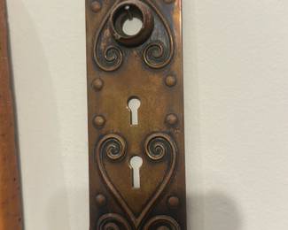 Ornate Brass Door Escutcheon Plate — Decorative ornate brass door escutcheon plate with scrollwork and two keyhole openings; the patinated finish shows age and character. Solid stamped brass (appears) with original mounting holes and a raised circular boss where a doorknob rose would sit. Good structural condition with surface oxidation and light wear consistent with vintage hardware; no major bends or breaks visible. Ideal for restoration or use on an older interior door; measures compactly and is an easy swap-in for period doors.