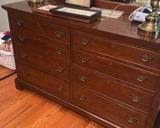Craftique Authentic Reproduction Dresser — This Craftique authentic reproduction dresser from Mebane, N.C. is a classic solid wood chest with a warm brown finish and brass bail handles. It features eight drawers with escutcheons, bracket feet, and a clean traditional silhouette ideal for a master bedroom. Measuring approximately 34 in high, 60 in wide, and 18 in deep, it offers substantial storage and a sturdy top surface for lamps and decor. Good used condition with surface scratches and light finish wear consistent with regular use; hardware and drawer function are intact.