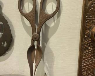 Candle Wick Trimmers — Decorative antique-style candle wick trimmers (scissors with built-in snuffer cup) in aged iron/steel with ornate engraved handles. Functional design trims and captures trimmed wick in the lower cup; shows an even rusted patina consistent with age and display wear but no broken parts visible. Good decorative collectible for a mantle or vintage tool collection; overall solid metal construction and measures like typical scissor-style wick snips.
