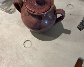 handmade glazed stoneware sugar pot — Small two-handled glazed stoneware sugar pot with lid, offered as a handmade pottery piece. The deep reddish-brown speckled glaze shows subtle variation and a glossy finish; form is rounded with two loop handles and a snug-fitting domed lid. No visible maker's marks or labels in photos; looks like studio pottery with normal surface wear and light glaze crazing expected from age and use. Compact size is suitable for tabletop use or as a decorative kitchen accent.