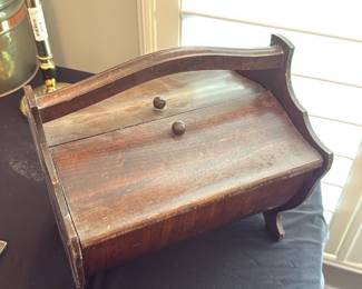 Antique Wooden Box — Small wooden stationery or recipe box with a hinged roll-top style lid and two wooden knob pulls. Constructed of stained hardwood with scalloped side panels and a curved carrying handle; interior shows wear and an old tape repair on the base. Solid but aged finish with surface scratches, scuffs and light losses to edges consistent with regular use. A compact decorative box suitable for desk storage or display; see photos for condition details.