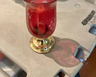 Cranberry Etched Glass Hurricane — Ruby-red blown glass hurricane with light etched floral/berry decoration and a polished brass-tone metal base. The flared rim and decorative etching give it a classic, decorative look suitable for tabletop or mantel display; the brass base is removable and shows minor surface wear. Overall condition is good with no visible chips or cracks in the glass from the provided photos; base has light surface scratches consistent with normal use. Measures as a medium decorative hurricane ideal for pillar candles or as an accent piece.