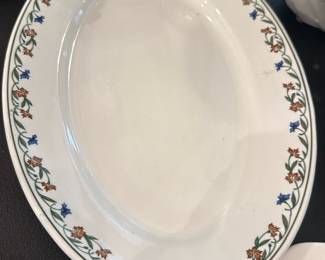 WF Daugherty Shenango China Platter — WF Daugherty & Sons Shenango China oval serving platter with a delicate green vine border and small blue and brown floral motif. Marked on the back "SHENANGO CHINA WF DAUGHERTY & SONS PHILADELPHIA"; hard-paste porcelain with a clean glazed surface and light surface wear consistent with use. Good solid piece for everyday service or display; no major chips or cracks visible in photos though there is minor surface scratching and light discoloration in the bowl. Measures as shown below and is a practical serving size for the dining table.