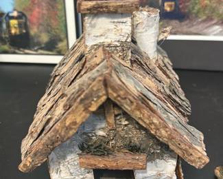 Handmade Birch Bark Cottage — Small handcrafted decorative cottage made from birch bark, twigs and natural moss. The piece features a pitched roof with layered bark shingles, a pointed steeple, small chimney and a doorway opening — a rustic accent suitable for shelf or tabletop display. Lightweight and clearly handmade with natural material variation; shows minor wear and a bit of separation at some bark edges consistent with age and handling. Measures compactly and is best used as a decorative collectible or seasonal vignette piece.