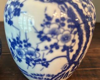 Blue & White Ginger Jar - Made in Japan — Decorative blue-and-white ginger jar marked "Made in Japan" on the base, a classic cottage-style porcelain piece ideal for mantel or shelf display. The jar features a rounded ovoid body with floral and tree motif transfer or hand-painted decoration and a matching domed lid. Estimated tabletop size makes it easy to place in a living room vignette; lightweight and portable for estate sale buyers. Good condition overall with minor rim glaze wear/age discoloration visible on the base and no obvious large chips or cracks.