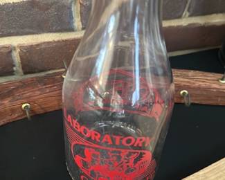 Laboratory Controlled Glass Carafe — Clear glass carafe with a narrow neck and flared lip featuring red screen-printed graphics reading "LABORATORY" and "CONTROLLED" around a central illustration. The piece is a decorative lab-style bottle or carafe suitable for display or use as a vase; print shows minor wear consistent with age and use but glass has no visible cracks. Sturdy thick glass construction and simple silhouette make it a functional accent for a sun room or tabletop display. Measures as noted below.
