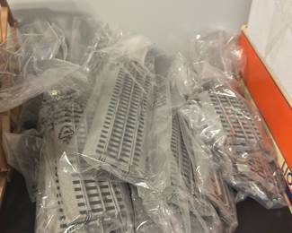 Lionel Train Tracks — Lot of Lionel train track sections in original plastic bags as shown. Pieces appear unused and include multiple straight and curved gray plastic track segments suitable for O gauge Lionel layouts. Good condition cosmetically with sealed packaging but not inventoried for count — sold as a grouped lot.