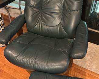 Stressless Dark Green Leather Recliner — This Stressless dark green leather recliner and matching ottoman offer ergonomic comfort with classic Scandinavian styling. Upholstered in dark green leather over a curved birch wood base, the chair features tufted padding, padded armrests and the Stressless tilt/locking mechanism. Chair with ottoman together measure approximately 40 in tall (chair), chair width 28 in, seat depth 20 in; ottoman footprint approx 18 x 14 in; solid wood base is sturdy and ideal for a living room. Shows signs of use with surface creasing and light scuffs on leather and base but structurally sound with working recline hardware.