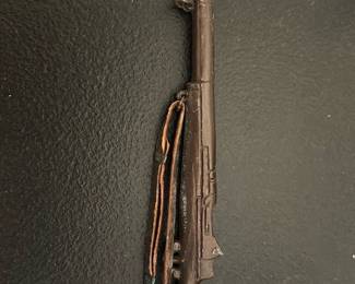 WWII Style Bayonet Rifle Toy — Small metal toy rifle with attached bayonet and cloth sling, modeled after a WWII-era service rifle. The piece appears to be a decorative or play item rather than a functional weapon — metal blade and cast metal stock with a stitched cloth sling. Shows surface wear and patina consistent with age and handling; no maker's marks or readable text visible in photos. Compact size makes it suitable for display with militaria or model collections.