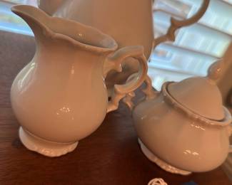 White Porcelain Creamer & Sugar Set — Two-piece white porcelain creamer and lidded sugar bowl with ornate loop handles and scalloped bases. Both pieces have a glossy white glaze with subtle molded rim and handle detailing; sugar bowl includes its fitted lid. Good collectible condition with light surface wear and no visible chips or cracks in photos. Sized for tabletop use with classic cottage or traditional table settings.