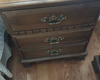 Wooden 3-Drawer Nightstand — Classic wooden 3-drawer nightstand with decorative brass-tone pulls and carved trim details. Constructed of stained wood with molded top edge and bracket feet, it offers three functional drawers for bedside storage. Measures approximately 28 inches high x 22 inches wide x 16 inches deep (see dimensions) and is a medium-weight piece suitable for easy home pickup. In good condition with light surface wear and minor finish scuffs consistent with normal use.