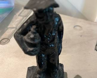 Coal Figurine — Small black painted metal figurine of a standing man wearing a hat and holding an object at his side, mounted on a square base. A metal maker's token is embedded in the underside of the base and reads around the edge "TOUR SPECIALITY ..." with a star in the center and the lower rim showing "COPYRIGHTED"; exact maker name is partially obscured. Surface shows heavy black paint with brush marks and light chips at edges consistent with age and wear. Stands roughly 4–6 inches high (see dimensions) and is a decorative shelf accent suitable for display or repair/ restoration.