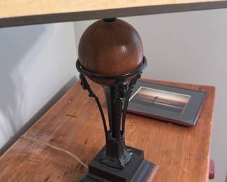 Art Deco Table Lamp Wood & Metal — Art Deco–style table lamp with a turned wooden finial and decorative metal tripod column on a stepped metal and wood base. The rectangular shade has a cream surface with black geometric border detailing; lamp shows expected surface wear and light scuffs to the base and shade consistent with age. Solid-feeling construction and decorative detailing make it suitable for a desk or side table; corded electric, working condition untested. Good overall condition with cosmetic wear as shown.