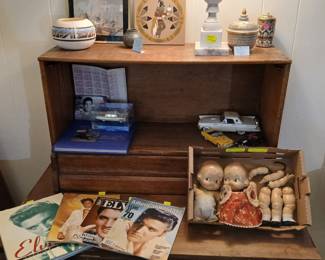 Elvis Presley Collection, Kewpie Dolls & Southwest Pottery Tags: Elvis Presley memorabilia, Elvis stamp sheet, Elvis Cadillac limousine model, Elvis magazines, kewpie dolls, antique bisque doll parts, Native American pottery, kachina art, marble lamp, diecast model cars A fantastic Elvis Presley collection: a full sheet of Elvis commemorative stamps, “The Family Album” book, an Elvis Presley 1960 Cadillac limousine model in display case, and vintage Elvis magazines and books including “His Personal Scrapbook” and “American Heritage.” Nearby, antique kewpie dolls and vintage bisque doll parts appeal to doll collectors, while diecast classic car models add variety. On top, Southwest-style pottery, a kachina sand painting, a marble lamp base ($40), and decorative ginger jars round out this eclectic and collectible-rich shelf.