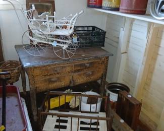 **Photo — Antique Door, Small Chest, Wire Buggy & Vintage Wagon** **Tags:** antique paneled door, small wood chest of drawers, wire doll buggy, zinc top table, vintage red wagon, tricycle, doll crib, Skelly oil cans A great architectural salvage piece — a solid wood paneled door — sits alongside a small chest of drawers and a rustic zinc-topped table. Nearby, the white wire doll buggy makes another appearance, along with a red vintage wagon, tricycle, and wood doll crib. Skelly Oil advertising tins are visible on the shelf above, tying together this room of primitive and childhood collectibles.