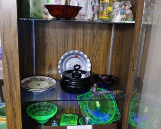Photo — Uranium Glass Collection (Glows Under Black Light!), Garfield Mugs & China Tags: vintage uranium glass, Vaseline glass, depression glass, black amethyst glass, Garfield collector mugs, Hummel figurines, china plates, black light glass A genuine showstopper: 1930s Depression-era uranium/Vaseline glass — including a scalloped compote, handled cake plate, and covered dish — that glows bright green under black light, shown here lit up. Also on this shelf: black amethyst glassware, crystal pieces, vintage Garfield collector mugs, floral china plates, and charming Hummel-style figurines. A must-see lot for depression glass and novelty collectors alike.