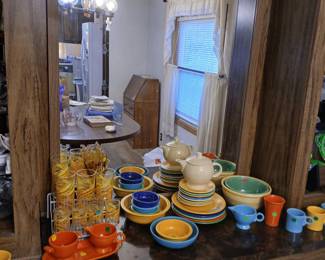 Photo — Vintage Fiestaware Collection & Retro Barware Tags: vintage Fiestaware, colorful ceramic dinnerware, Fiesta bowls plates and teapots, mid-century gold swirl glasses, creamer and sugar sets, retro tumblers, collectible pottery dishes A wonderful collection of vintage colorful Fiestaware-style dinnerware: stacks of plates and bowls in classic yellow, cobalt, turquoise, and orange, plus matching teapots, creamers, and mugs. Alongside, a set of retro gold swirl drinking glasses in a wire caddy adds mid-century flair — a fantastic find for Fiesta collectors looking to build or complete a set.