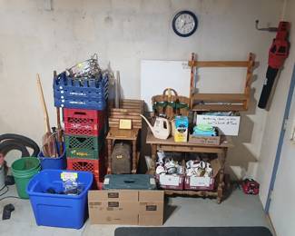 Photo — Vintage Milk Crates, Wood Table, Mugs & Gardening Lot Tags: vintage milk crates, Pepsi crate, dairy crate, wood side table, coffee mugs, gardening tools, watering can, wicker gardening basket, tool box, Skil battery, wall shelf Great vintage milk crates from Hiland Dairy and Steffen’s stacked on a Pepsi-Cola crate — perfect storage or display pieces for collectors. A small wood table holds a watering can, Miracle-Gro, and a wicker gardening tool basket, with gardening items priced at $1 each and microfiber cloths at 50¢. Below, boxes of collectible coffee mugs, a tackle box, and a Skil battery/tool add to this practical household lot.