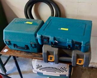 Makita Power Tool Cases & Small Pet Carrier Tags: Makita hard case tool boxes, power tool storage cases, coiled hose, small pet carrier, garage tool organization Sturdy hard-shell Makita power tool cases in teal, great for organizing and transporting cordless tools — a coiled black hose sits behind them. Below, a small plastic pet carrier rounds out this practical lot for garage or workshop storage.