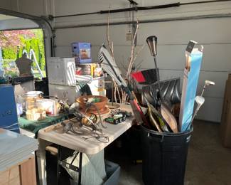 Garage is loaded with tools, garden flags, light fixtures, chest, garden tools, misc. yard chemicals, power tools, decor, paint, spray paint, shovels, brooms, work bench, storage lockers, pots, planters, decorations, tile saw, sprinkler system parts, new garden gloves, etc.