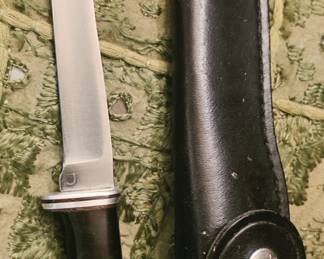This is a vintage Buck Model 121 Fisherman fixed-blade knife with its original Buck leather sheath. The black phenolic handle, aluminum fittings, and narrow upswept blade match that model. �